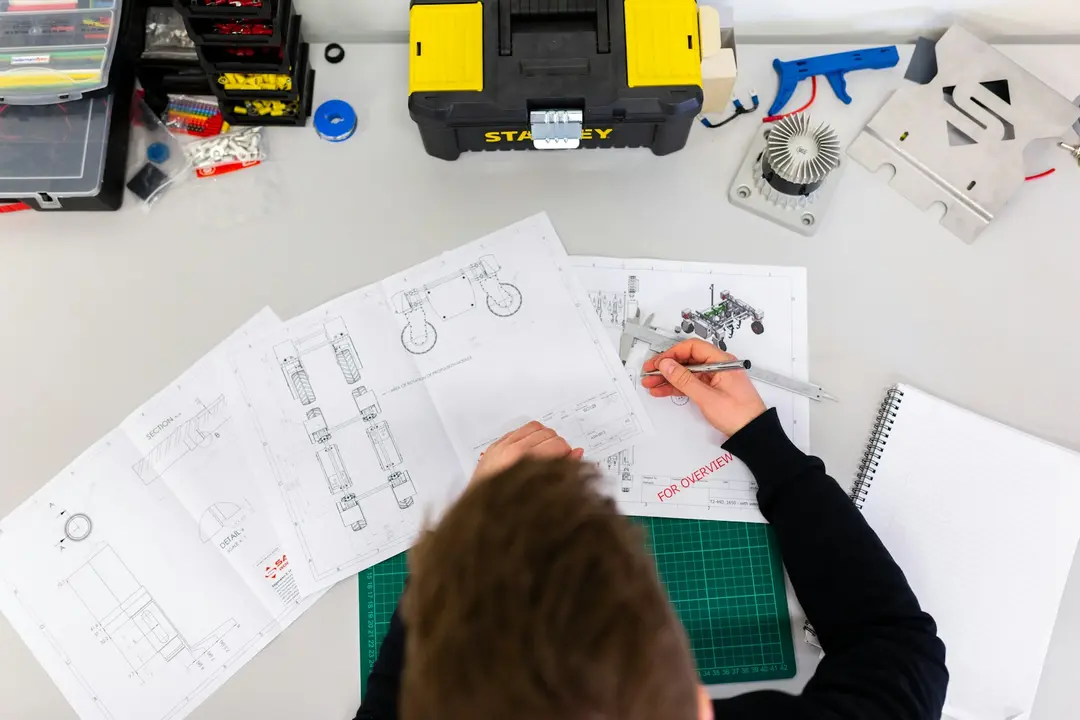 Profissional desenhando um projeto técnico sobre a mesa com ferramentas ao lado